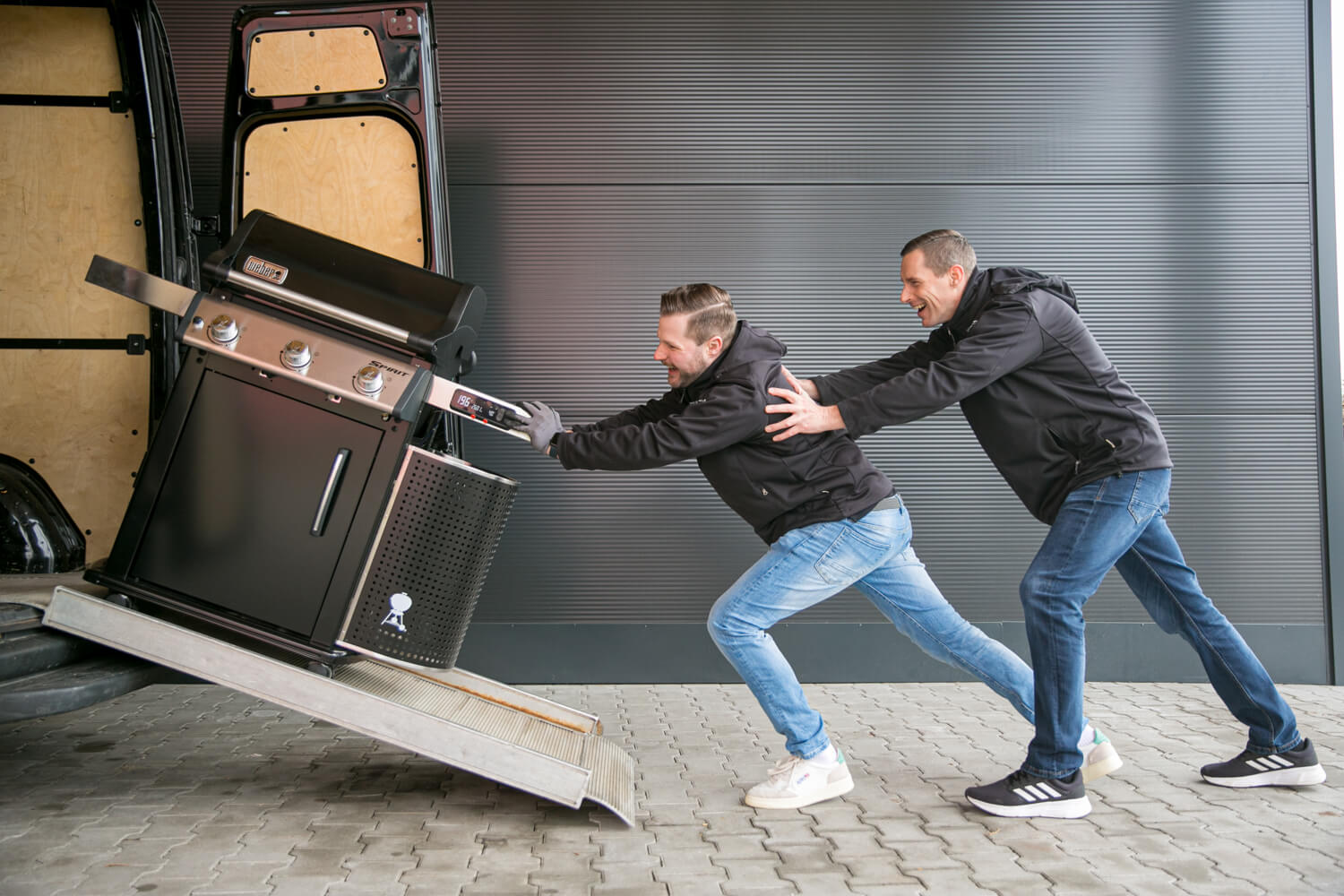 Zwei Männer schieben einen Weber Grill in einen Transporter